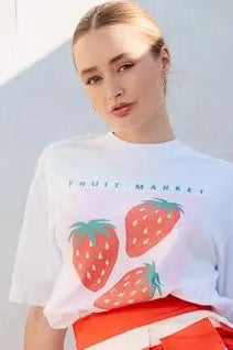 Person wearing a white t-shirt with strawberry graphics on a plain background