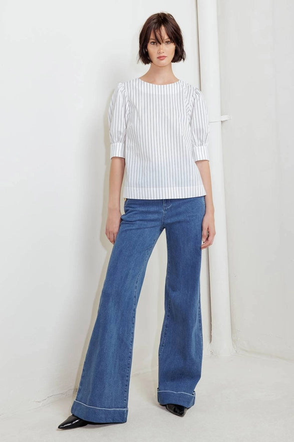 Woman wearing a white blouse and blue jeans against a plain background
