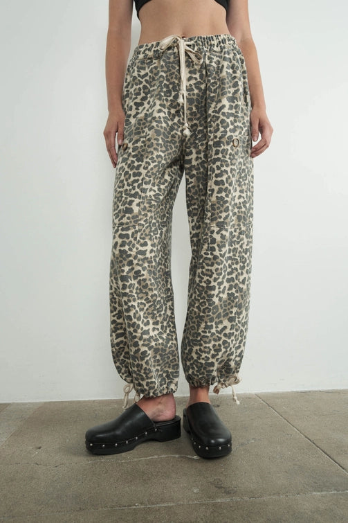 Person wearing leopard print pants and black clogs on a plain background