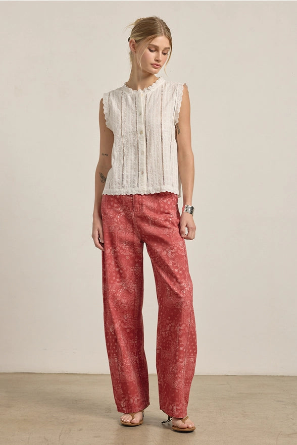 Woman wearing a white sleeveless top and red patterned pants against a plain background