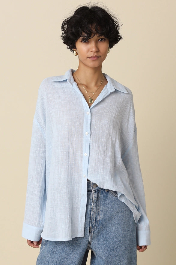 Woman wearing a light blue button-up shirt and jeans against a beige background