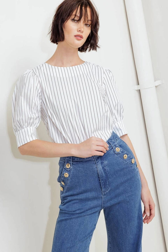 Woman wearing a white striped shirt and blue jeans against a plain background