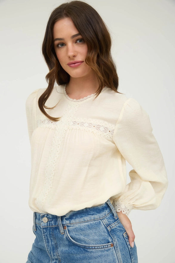 Woman wearing a cream blouse with lace details and blue jeans against a white background