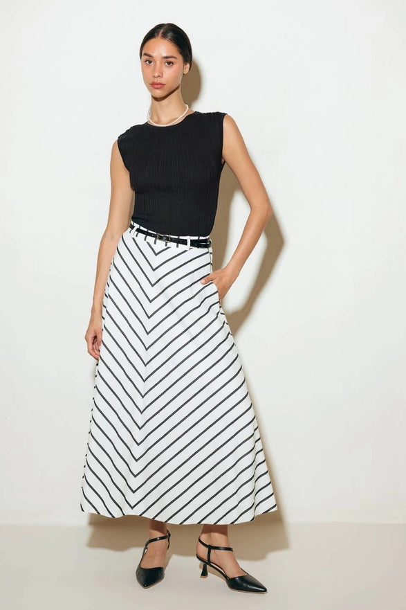 Woman wearing a black sleeveless top and a long black and white striped skirt on a white background