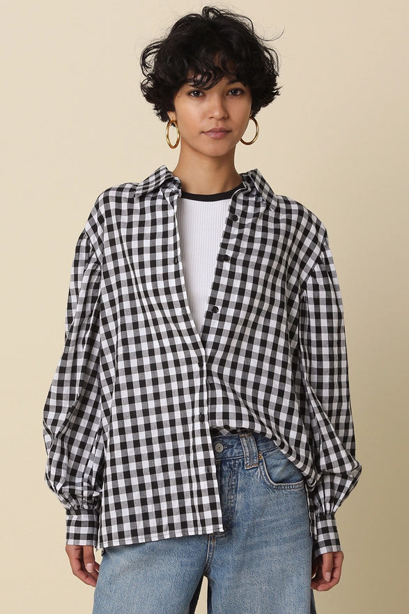 Person wearing a black and white checkered shirt over a white top with blue jeans on a beige background