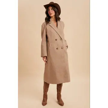Woman wearing a beige trench coat and brown hat on a beige background