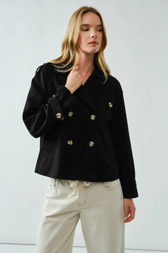 Woman wearing a black coat with gold buttons against a white background