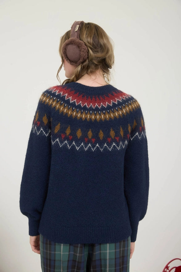 Person wearing a navy blue sweater with a colorful pattern, standing against a plain background.