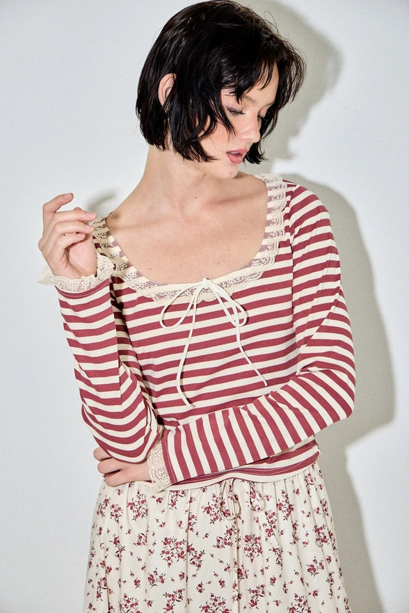 Woman wearing a red and white striped top with lace details against a plain background