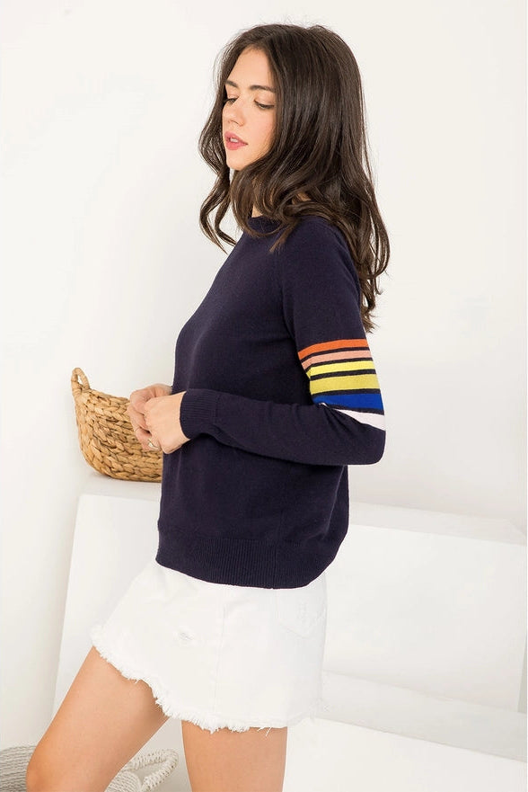 Woman wearing a navy sweater with colorful sleeves and a white skirt, holding a woven basket.