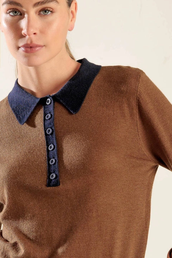 Woman wearing a brown sweater with a blue collar against a plain background