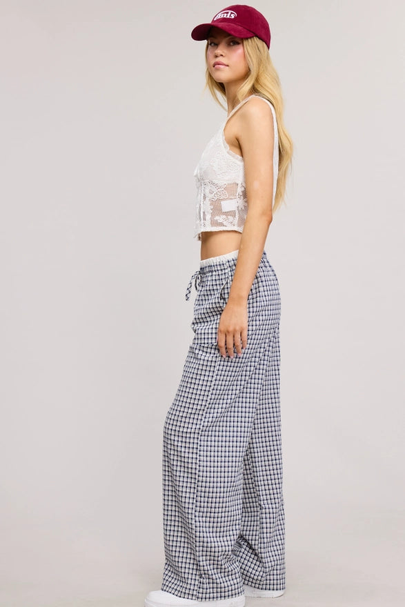 Person wearing a white lace top and checkered pants with a red cap on a plain background