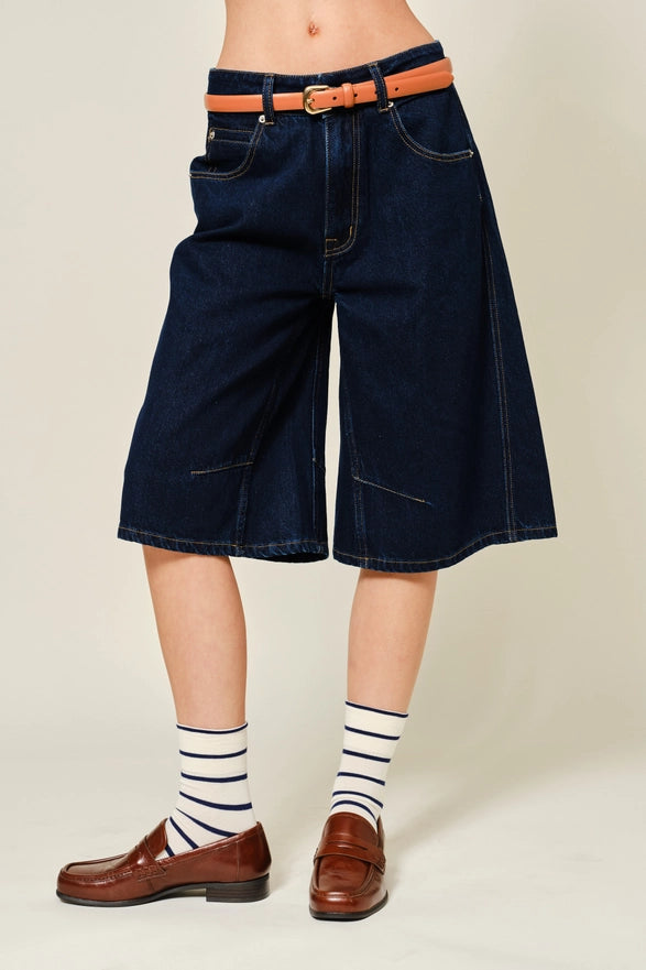 Person wearing dark blue denim shorts, striped socks, and brown shoes on a beige background