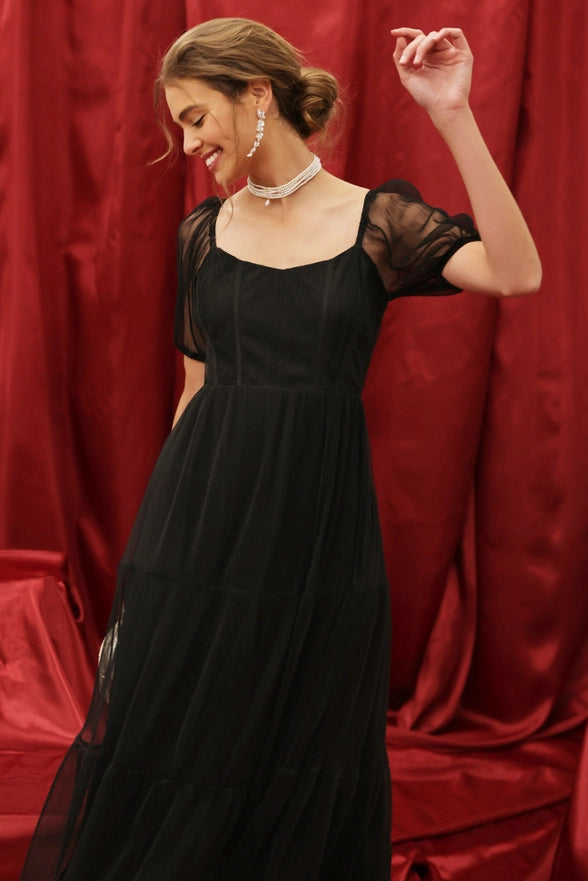 Woman in a black dress posing against a red curtain