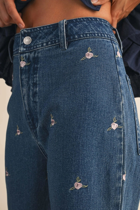 Close-up of blue jeans with floral embroidery on a neutral background