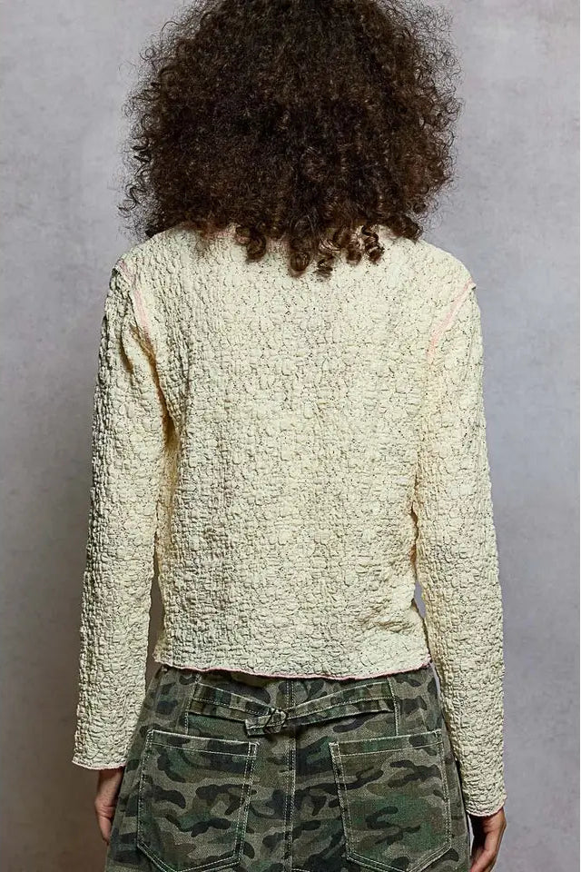 Person wearing a textured white sweater and camouflage pants against a gray background