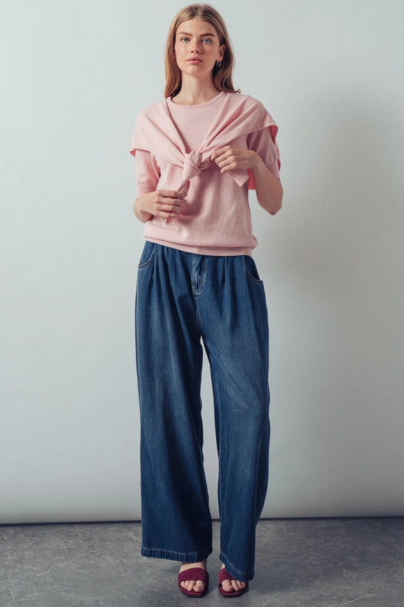 Woman wearing a pink top and blue jeans against a plain background