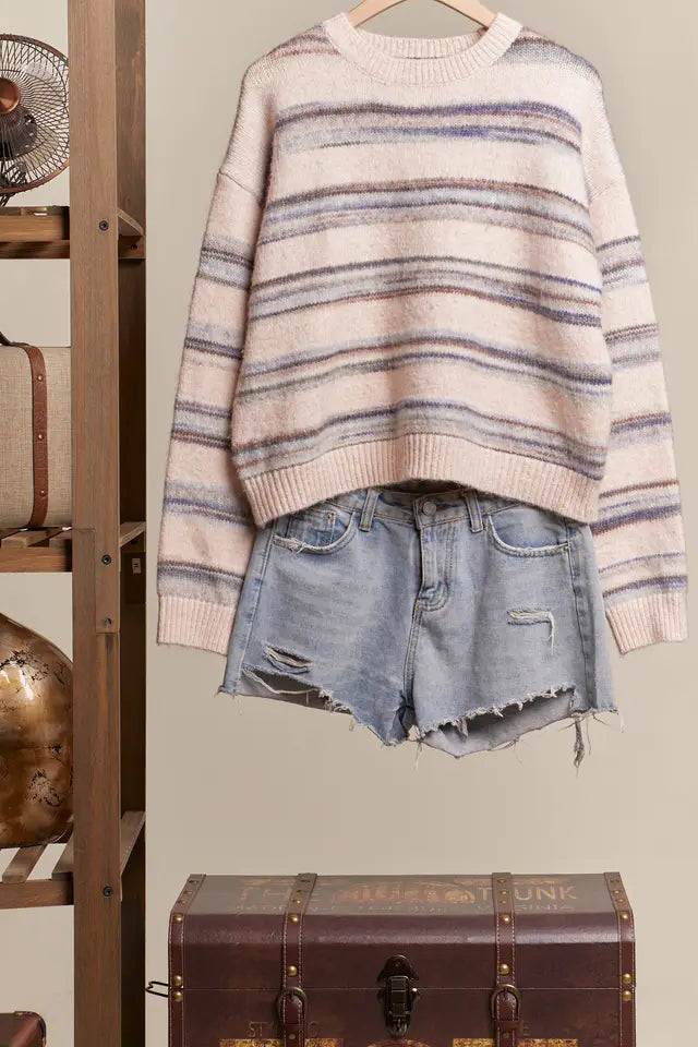 Striped sweater and denim shorts on a hanger against a neutral background with a wooden shelf and trunk.