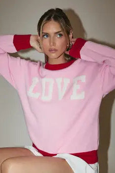 Person wearing a pink sweatshirt with 'LOVE' printed on it against a plain background