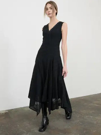 Woman wearing a black dress standing in a minimalistic room with white walls and a concrete floor.
