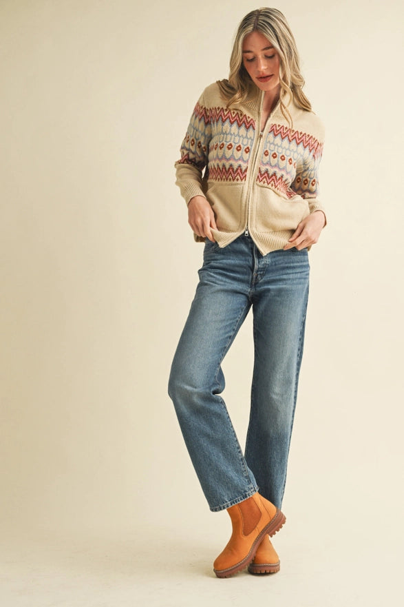 Woman wearing a patterned sweater, jeans, and boots on a plain background