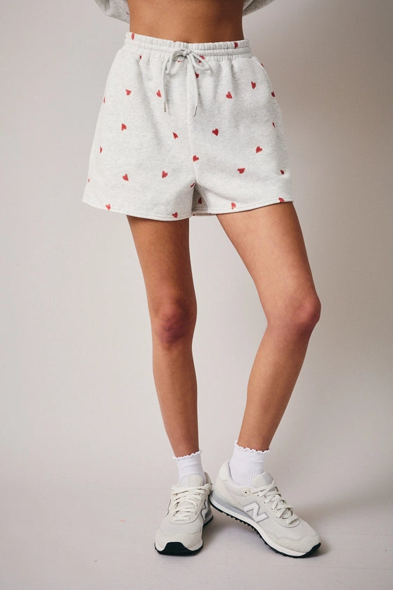 White shorts with red heart pattern worn by a person on a plain background