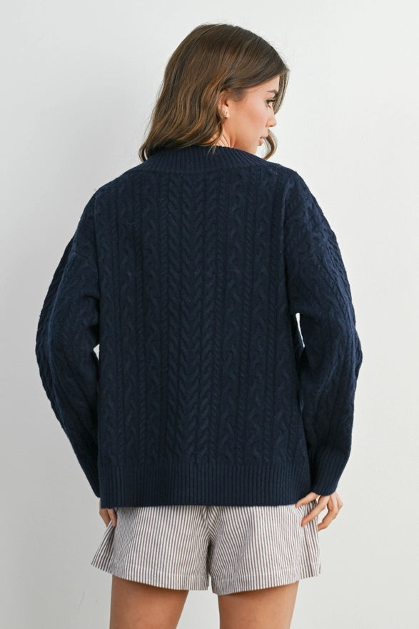 Girl Standing against a plain background wearing a V neck Navy Blue cable knit sweater with long sleeve