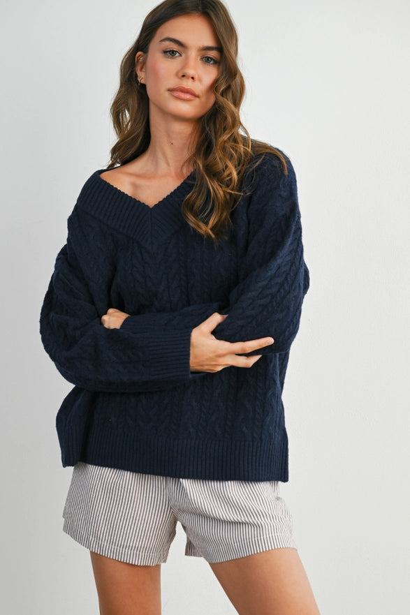 Girl Standing against a plain background wearing a V neck Navy Blue cable knit sweater with long sleeve