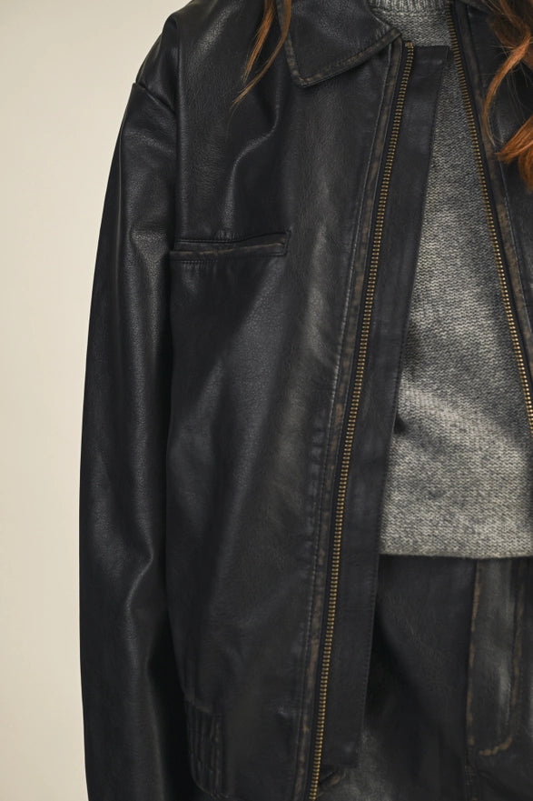 Close-up of a black leather jacket with a zipper, worn over a gray sweater.