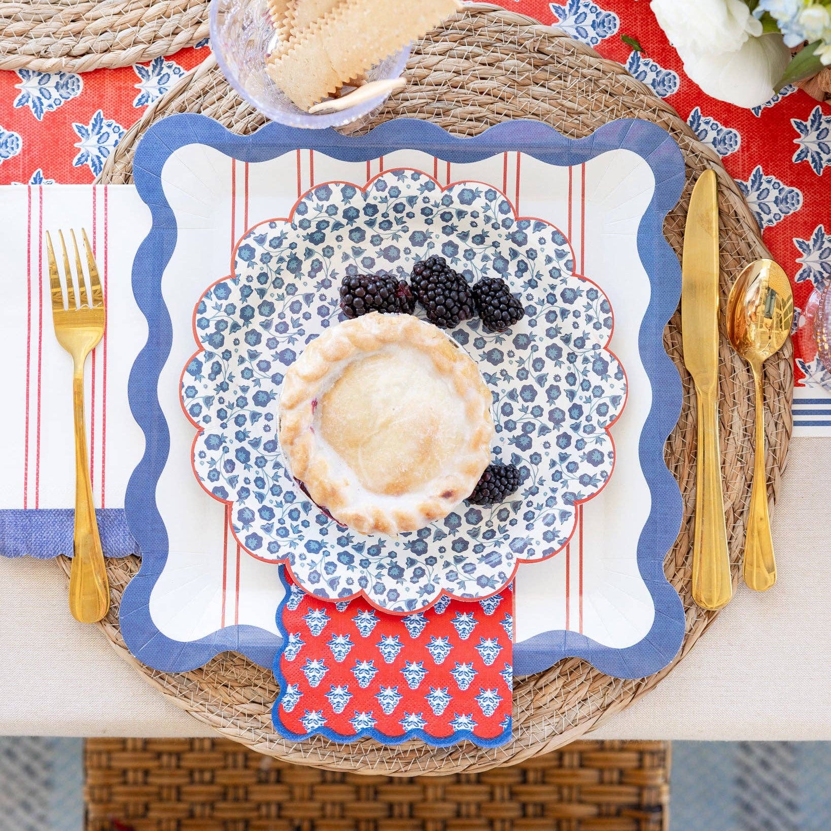 Decorative placemat with a pie and blackberries on a table setting with cutlery and a bowl of cookies.