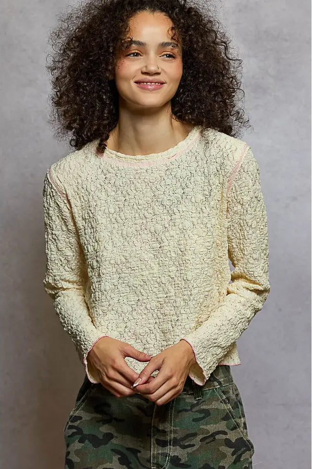 Person wearing a textured cream sweater and camouflage pants against a gray background