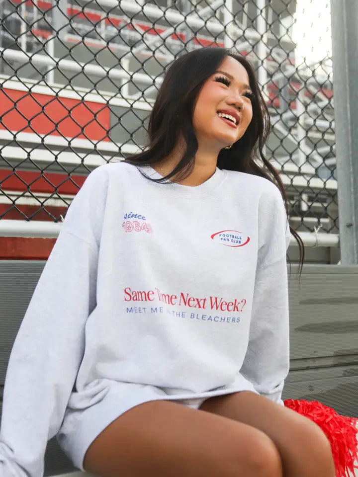 Person wearing a sweatshirt with text sitting on bleachers.