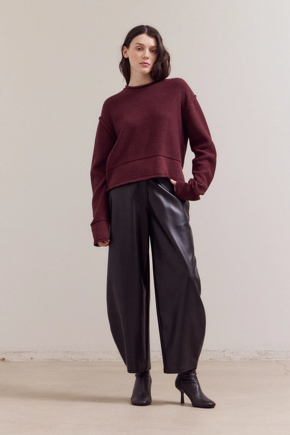 Person wearing a burgundy sweater and black pants against a plain background