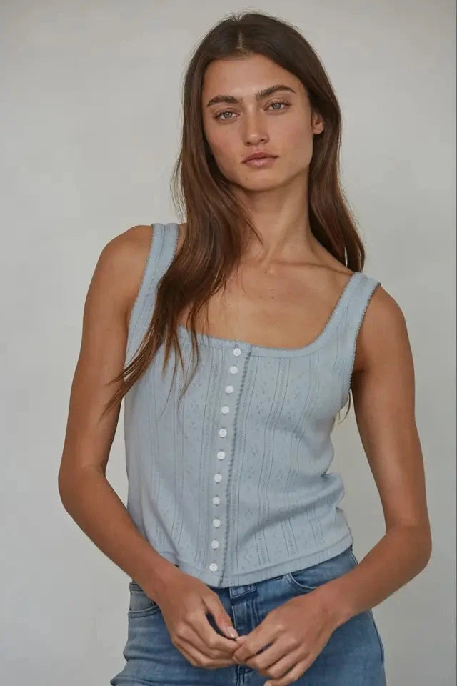 Woman wearing a light blue tank top with buttons against a plain background