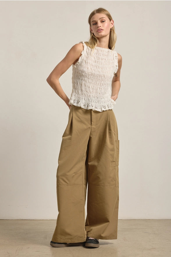 Woman wearing a white top and beige pants against a plain background