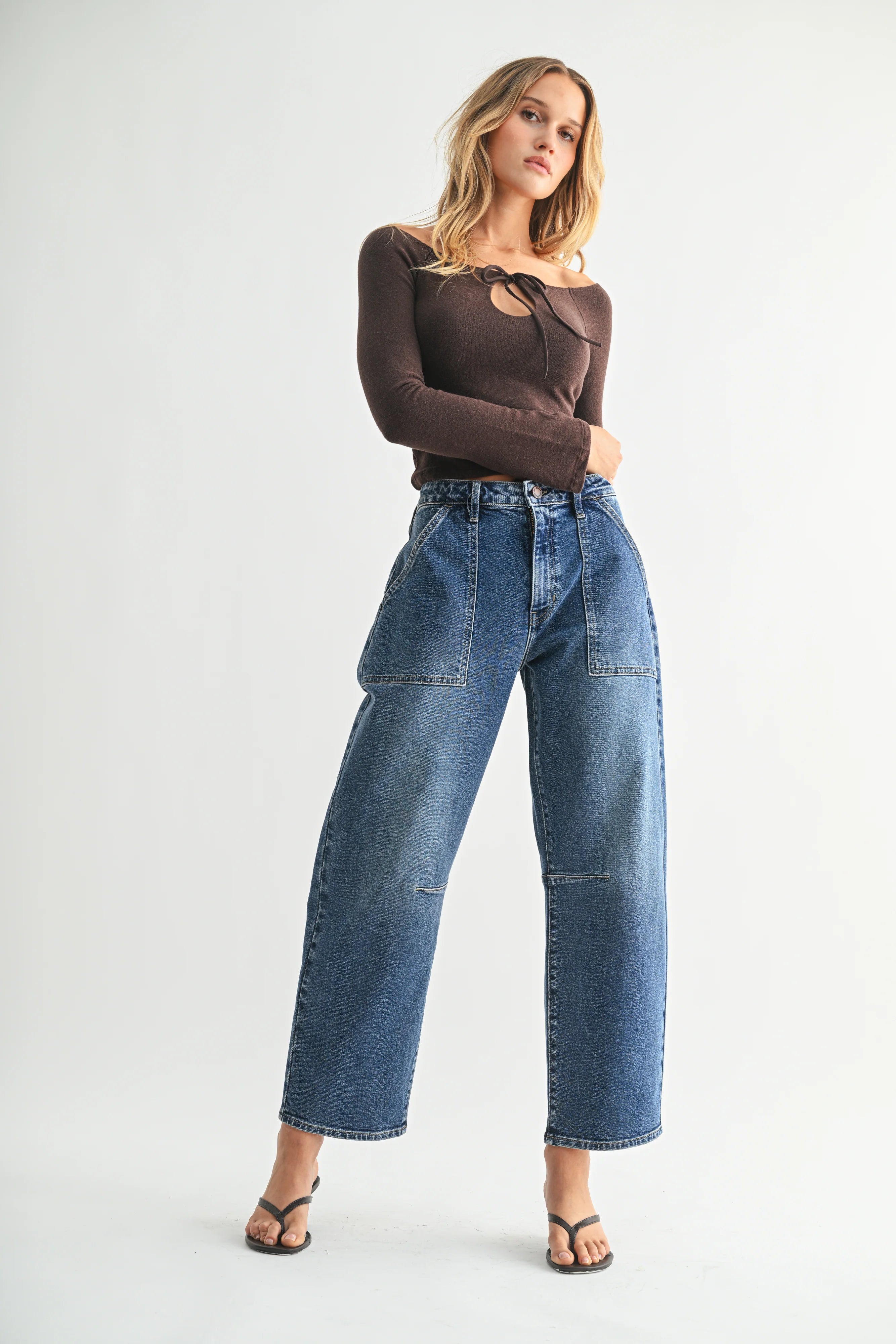 Woman wearing a brown long-sleeve top and blue jeans on a white background