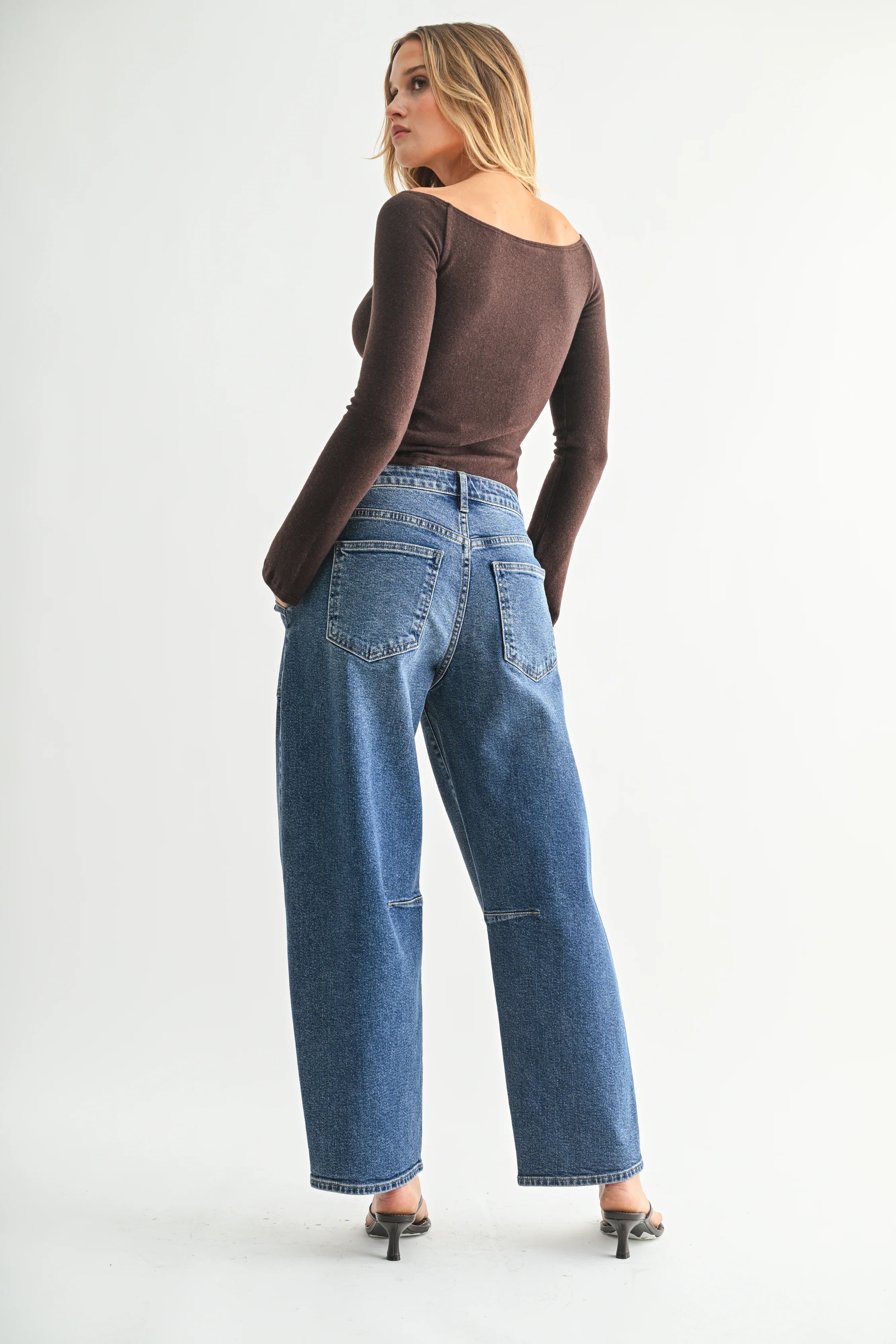 Woman wearing a brown long-sleeve top and blue jeans on a white background
