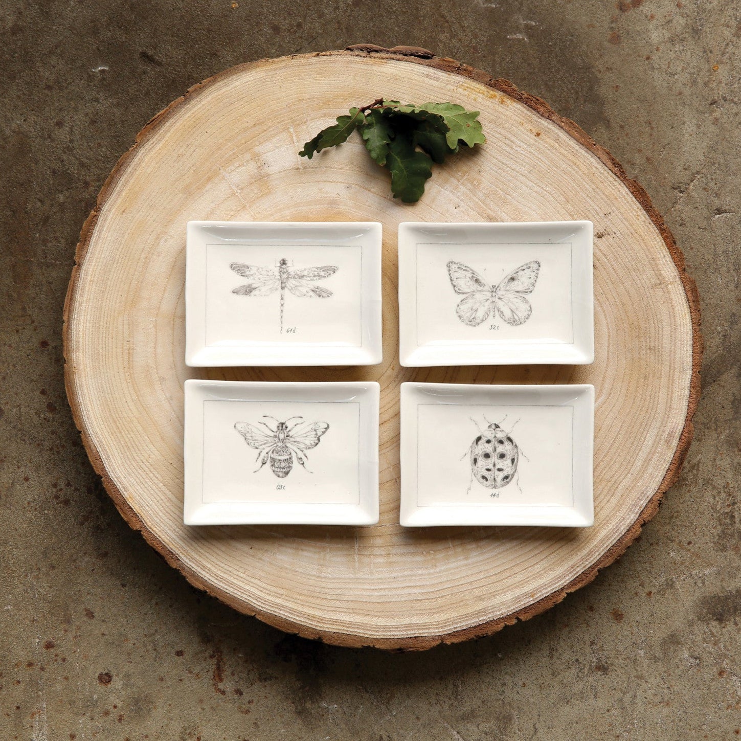 Set of four square ceramic plates with nature-themed designs on a wooden circular board.