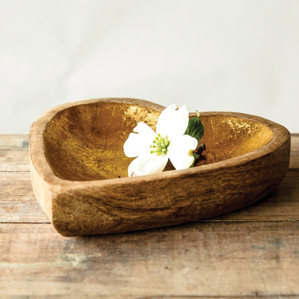 Heart-shaped wooden bowl with a white flower on a wooden surface