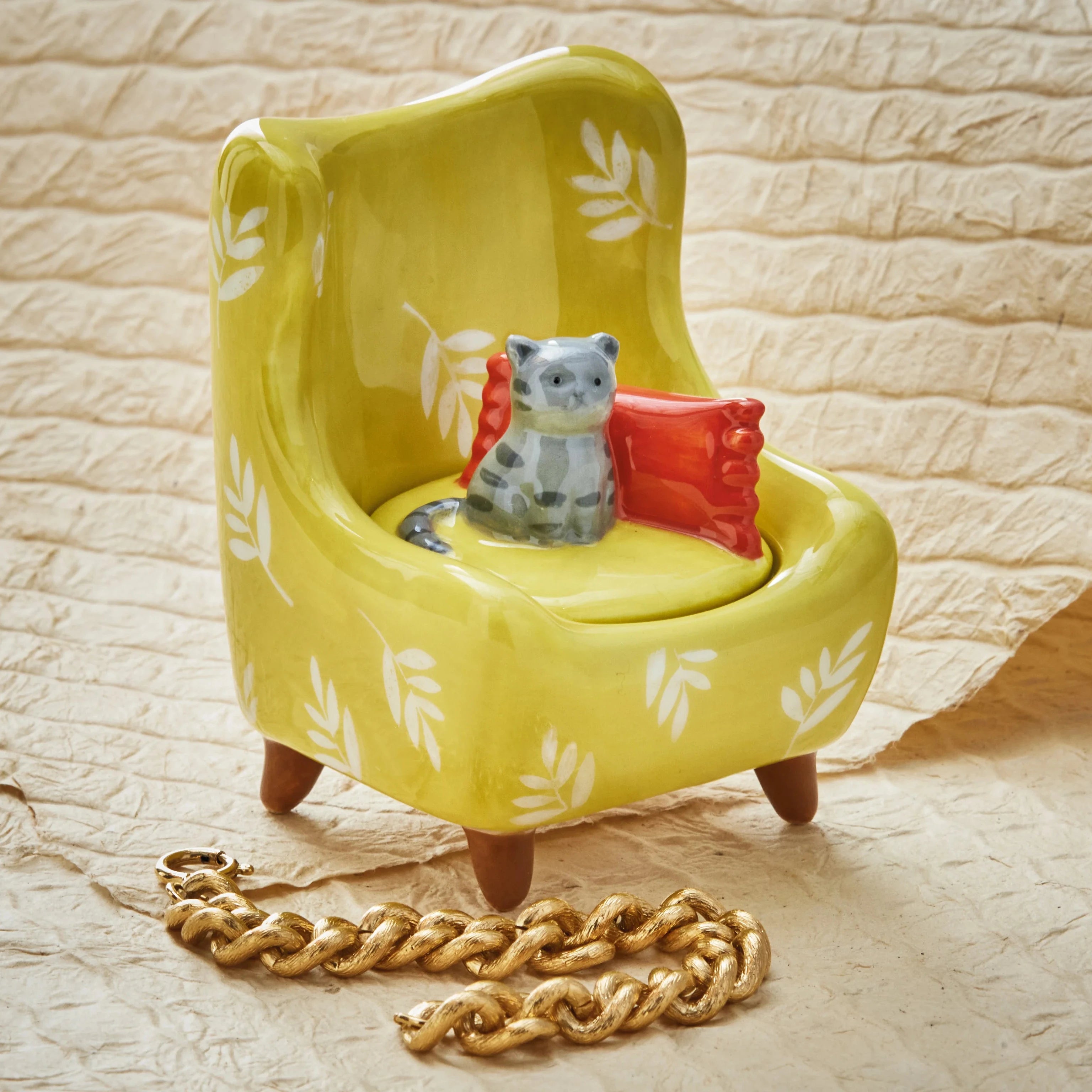 Yellow chair with a small cat figurine and red cushion on a textured beige surface.