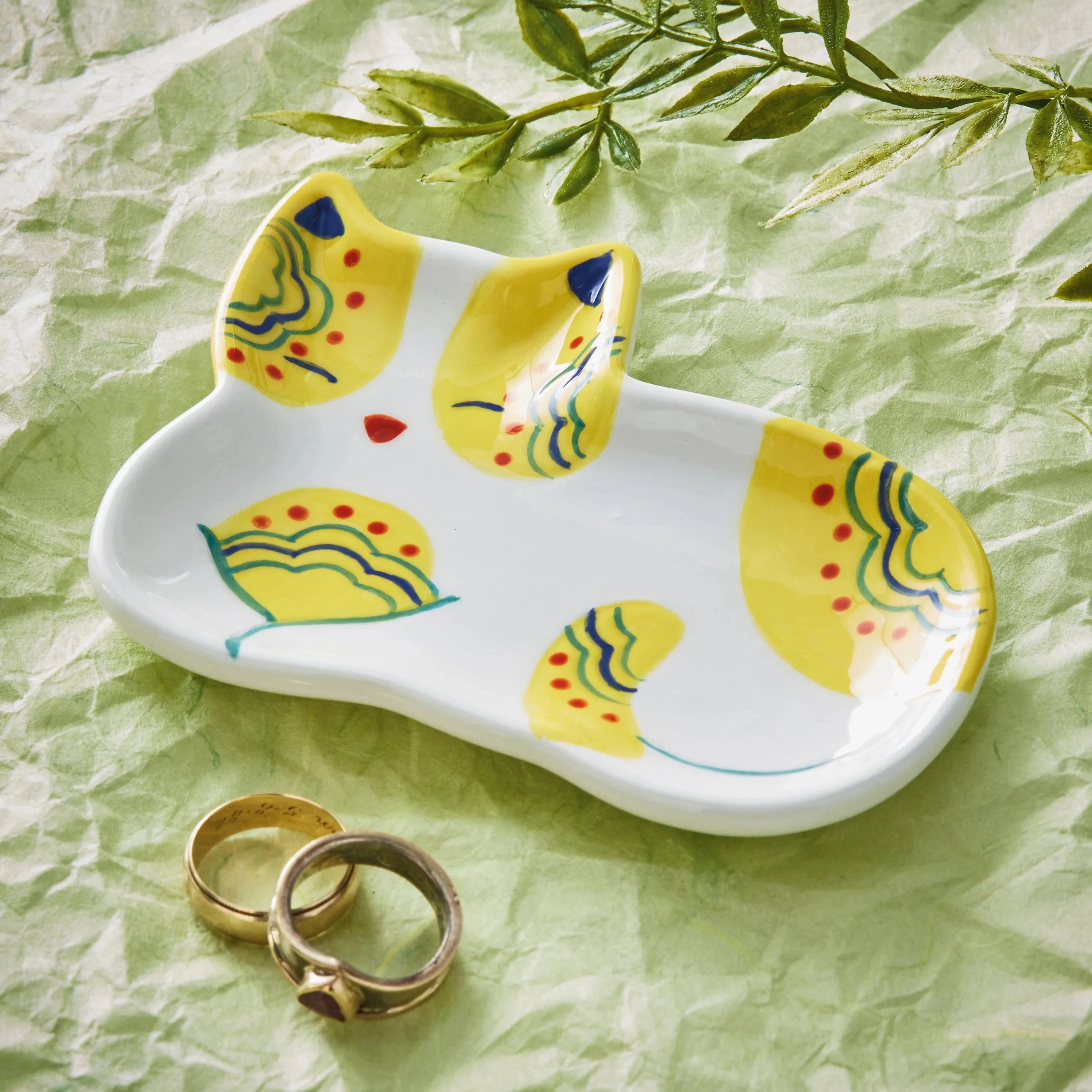 Ceramic cat-shaped trinket dish with decorative patterns on a green crumpled paper background.