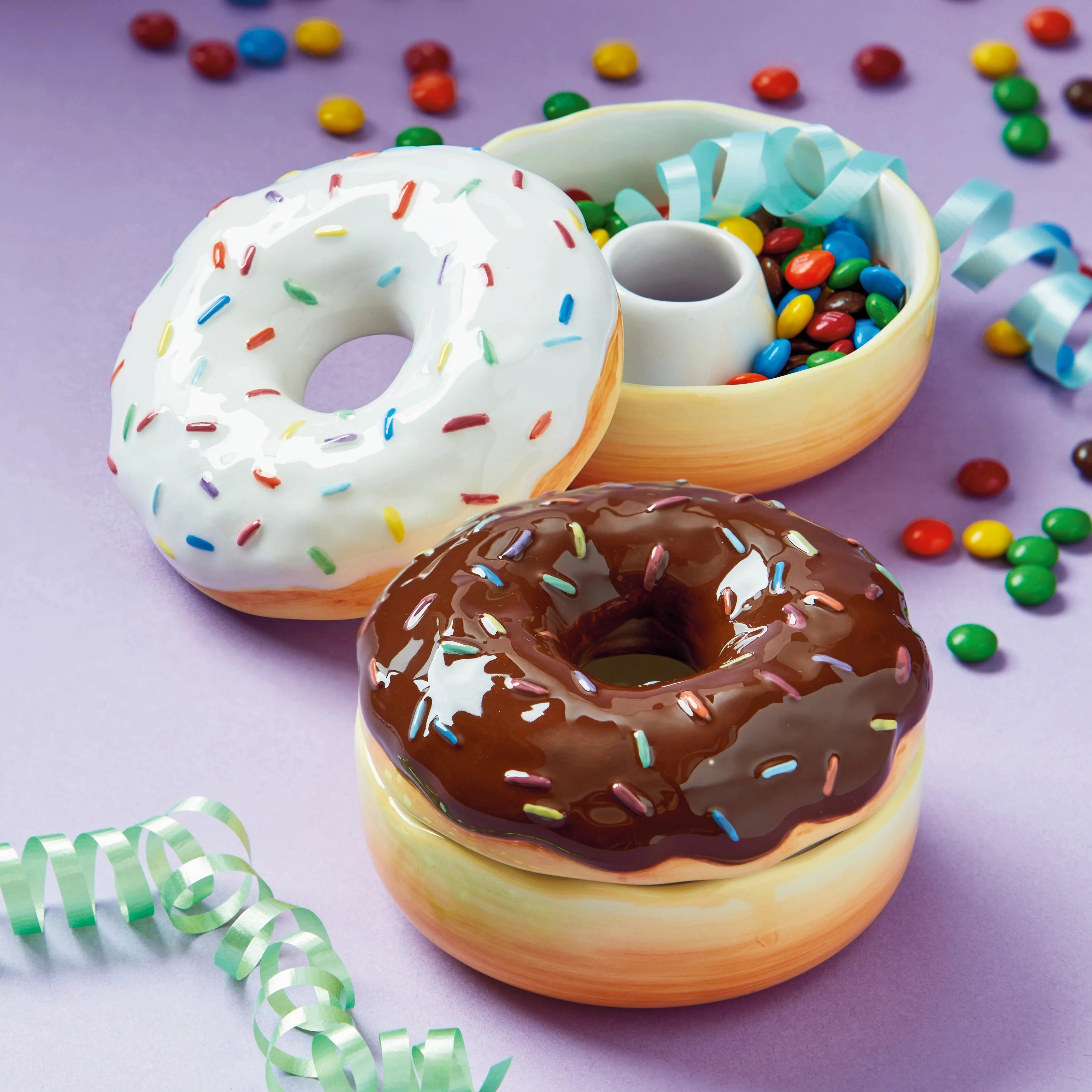 Two donut-shaped containers with colorful sprinkles and candies on a purple background