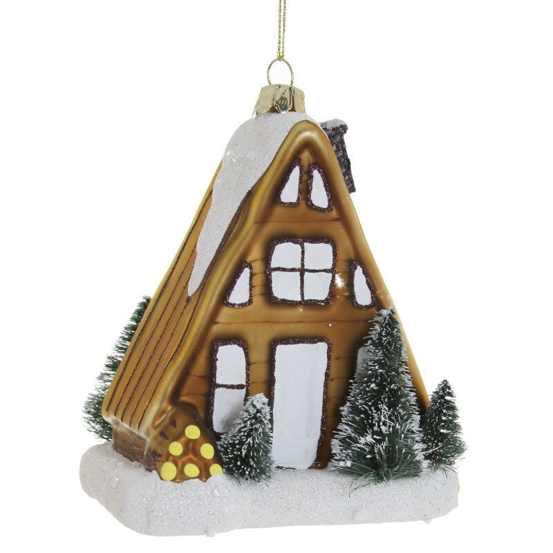 Decorative Christmas ornament of a wooden cabin with snow and trees on a white background