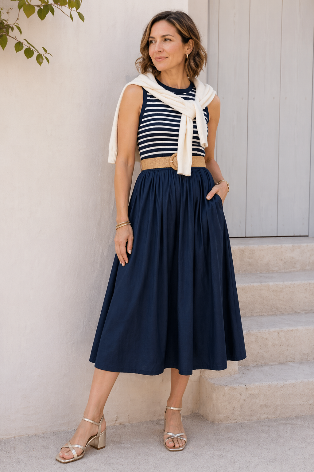 Woman wearing a striped top and navy skirt standing on steps with a neutral background