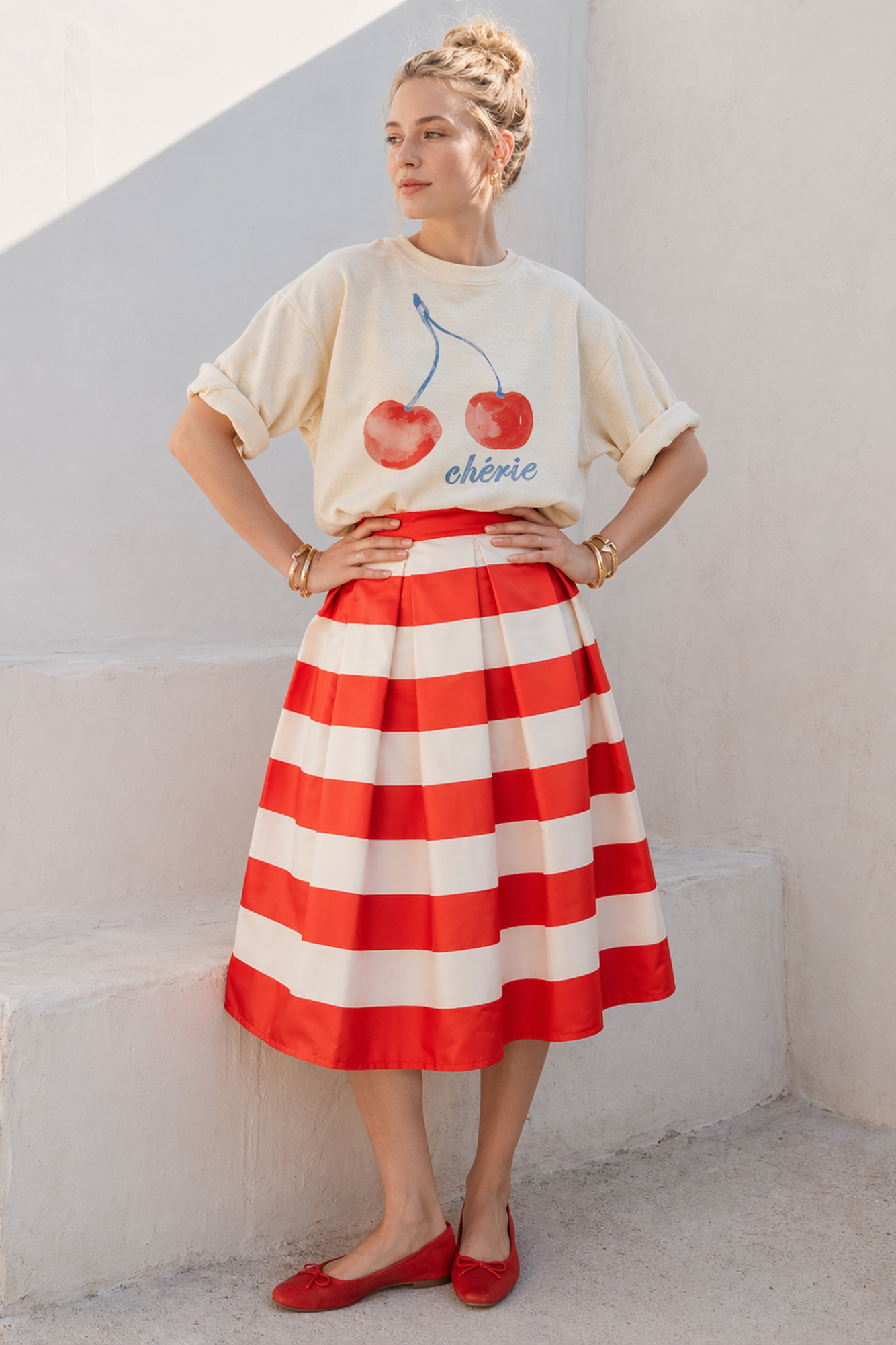 Woman wearing a graphic t-shirt and red and white striped skirt against a light-colored wall.