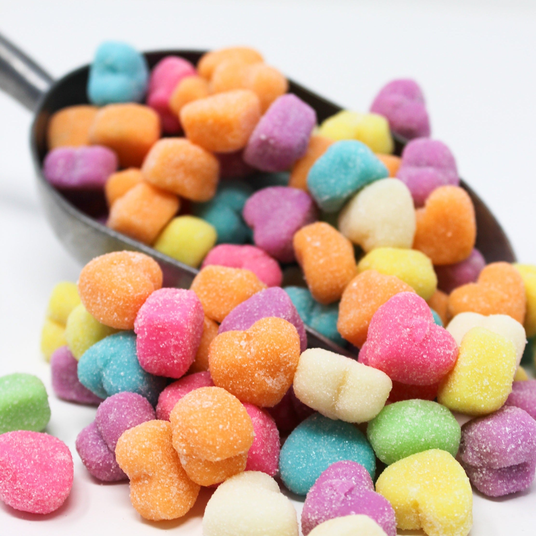 Gummy heart candy with purple, pink, blue, white, orange coming out of a scoop. 
