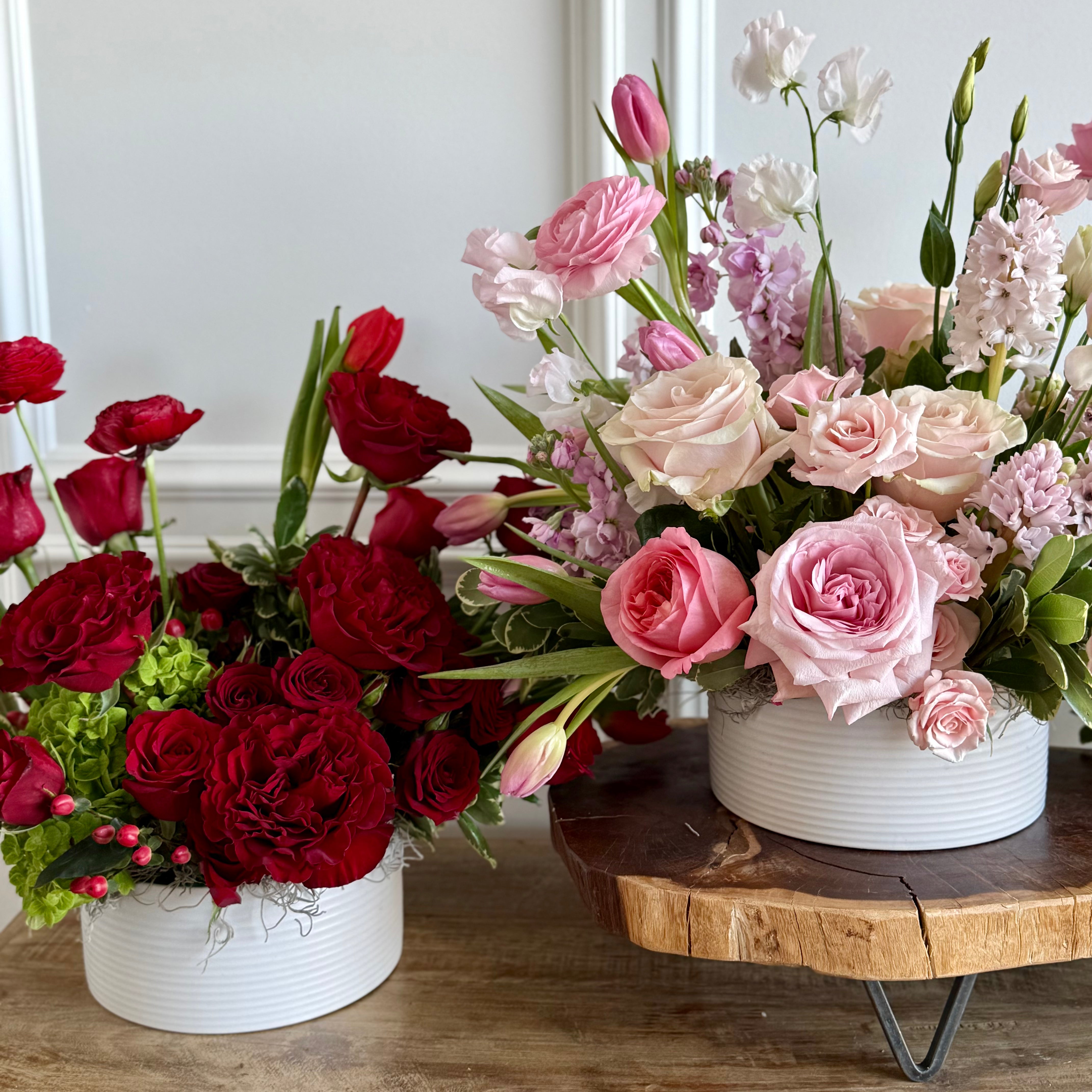 Three flower arrangements in white containers on a wooden surface.