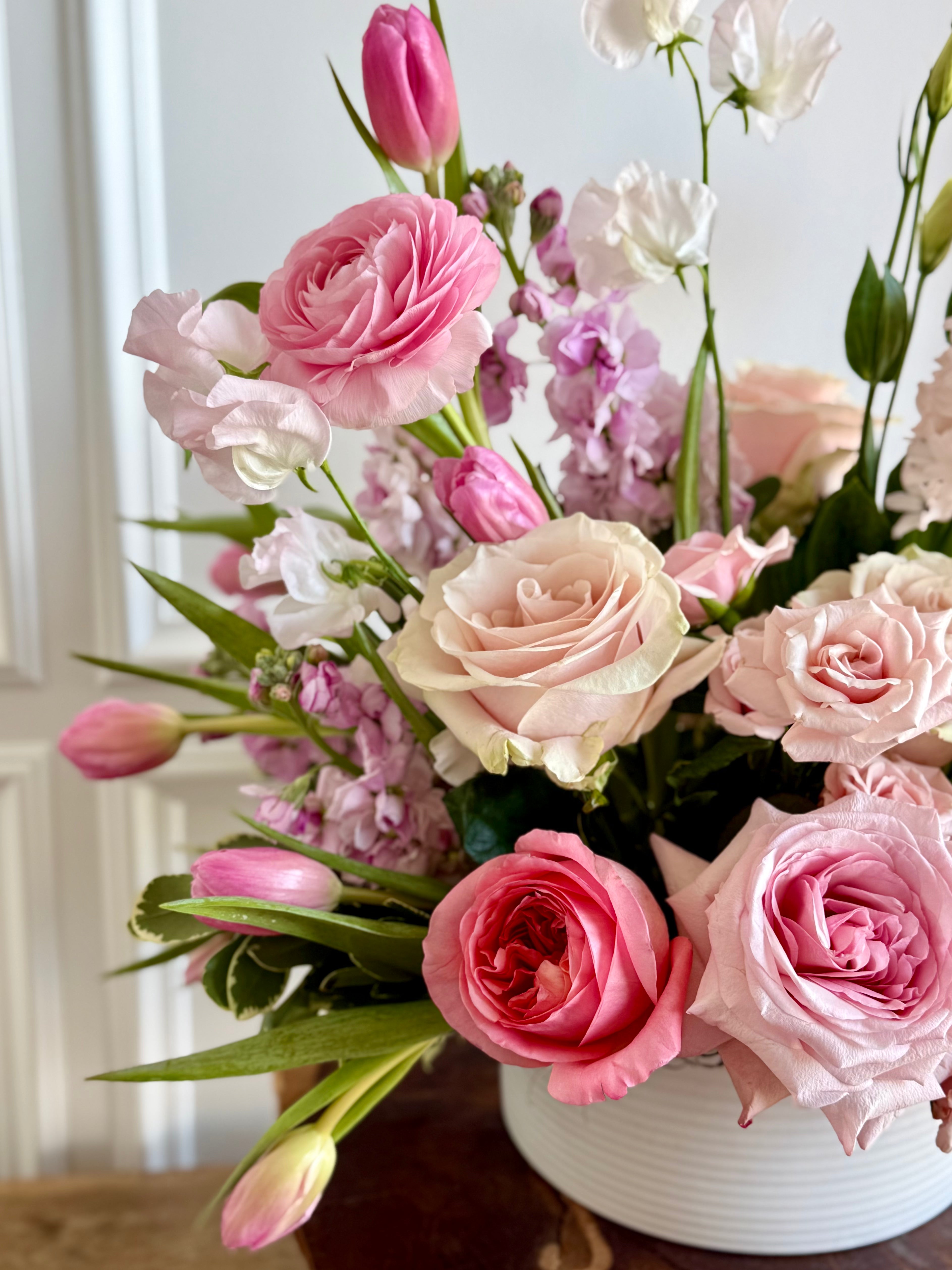 Bouquet of pink and white flowers in a white vase on a wooden surface.