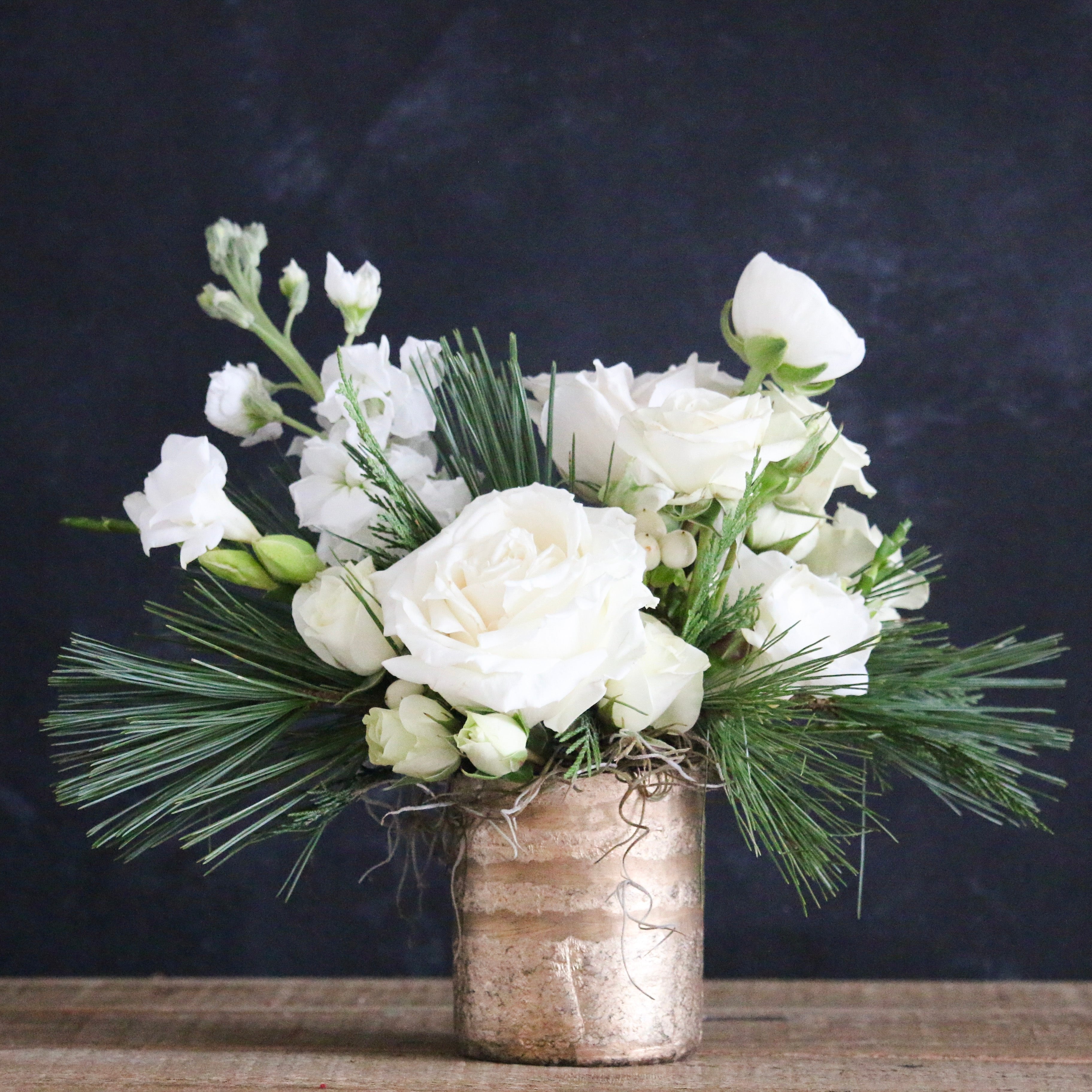 A floral arrangement featuring white roses and green foliage in a silver metallic vase.
