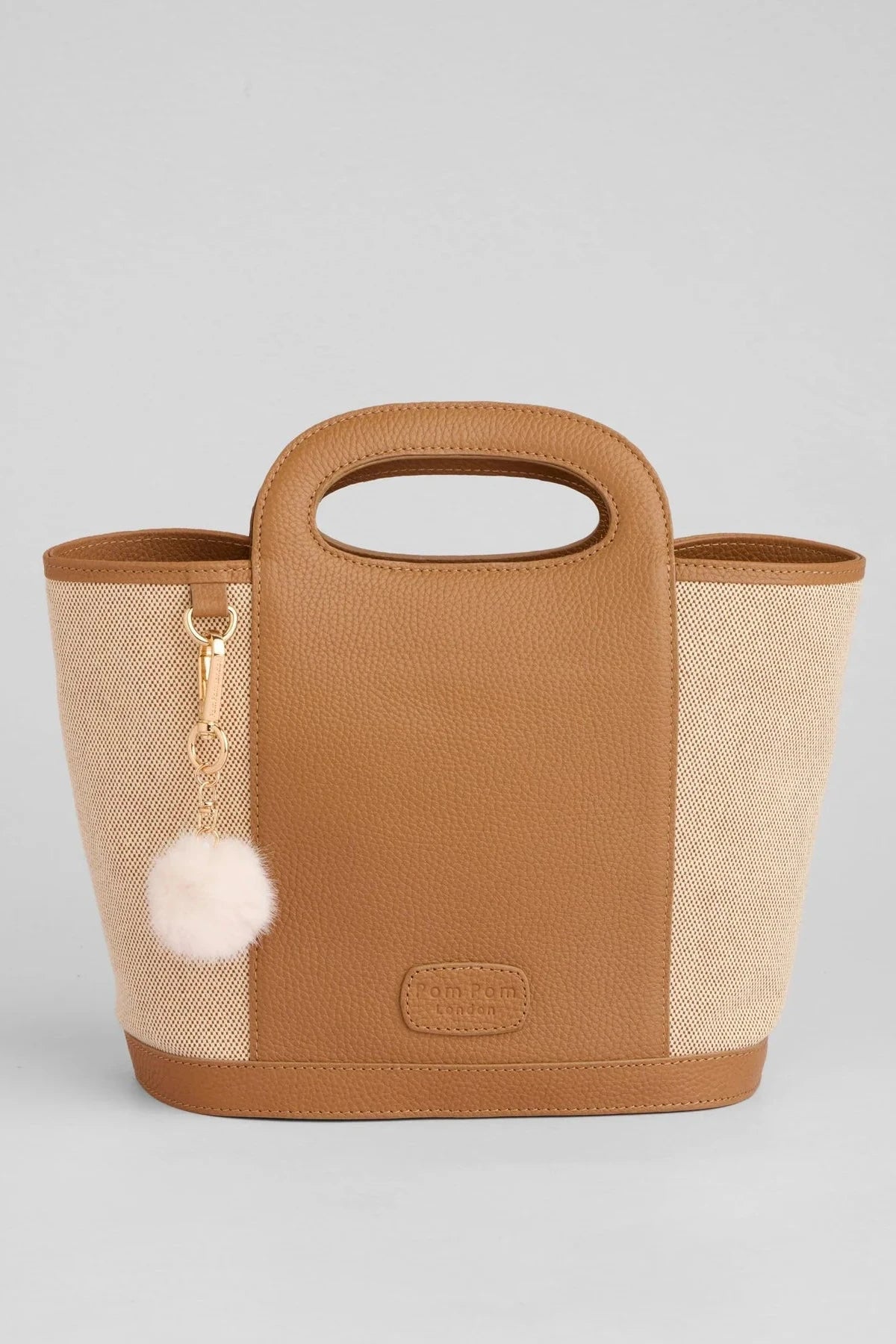Beige and brown handbag with a pom-pom keychain on a light gray background